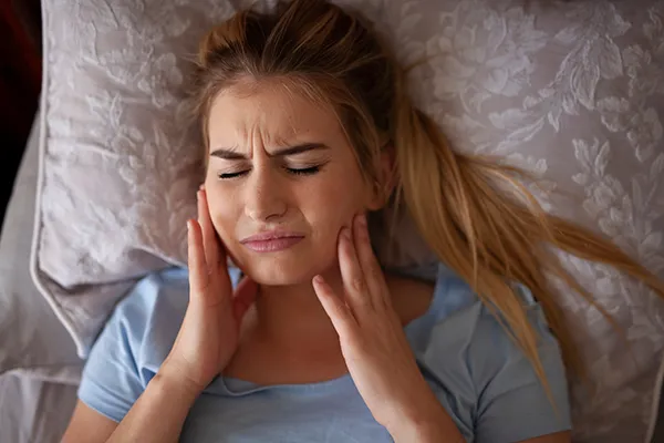 patient with pained facial expression rubbing her jaw while in bed