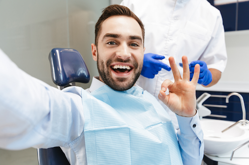 happy male patient in the dental chair giving an 'okay' sign with his hand that he is healing from oral surgery