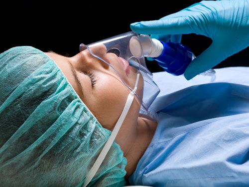 Dr. Djawdan's gloved hand holds breathing mask to sleeping patient's face