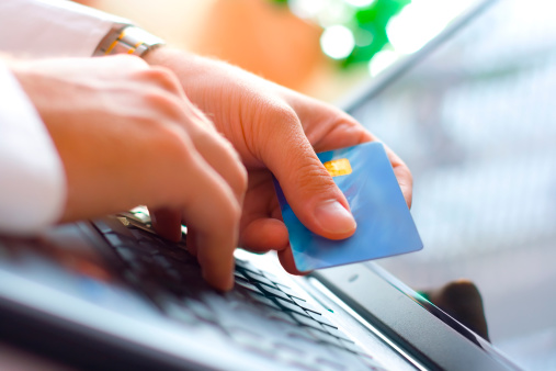 A hand holding a card in front of laptop